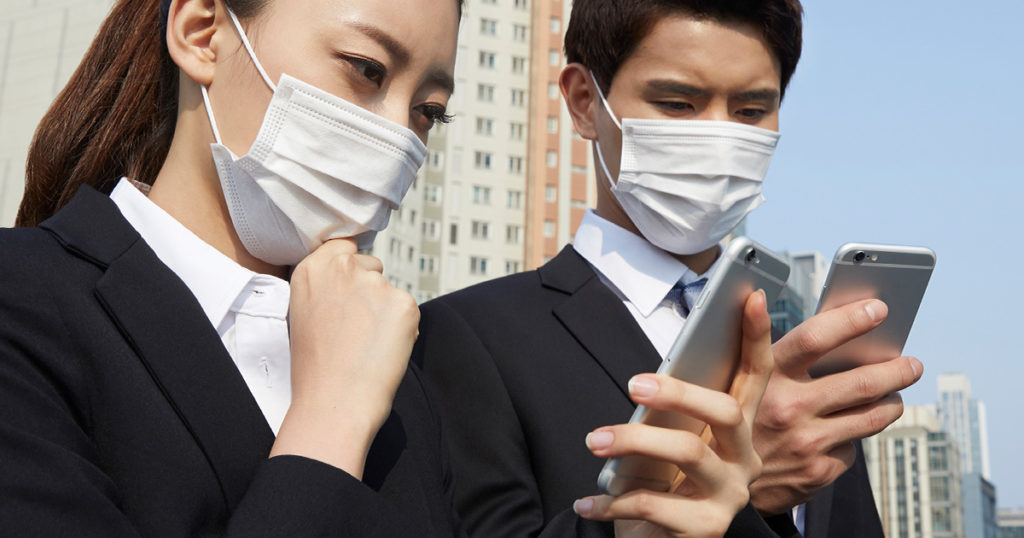 マスクを着用してスマートフォンを凝視するビジネスマンの写真